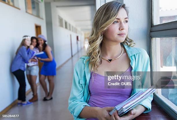 student looking out window, friends gossiping in background - friends loneliness foto e immagini stock