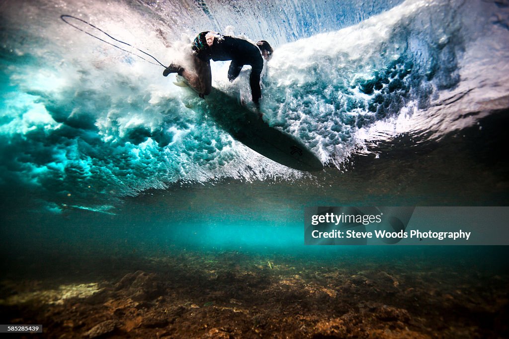 Underwater view of surfer falling through water after catching a wave on a shallow reef in Bali, Indonesia