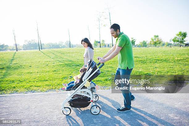 mid adult couple and toddler daughter in pushchair strolling in park - 乳母車 ストックフォトと画像