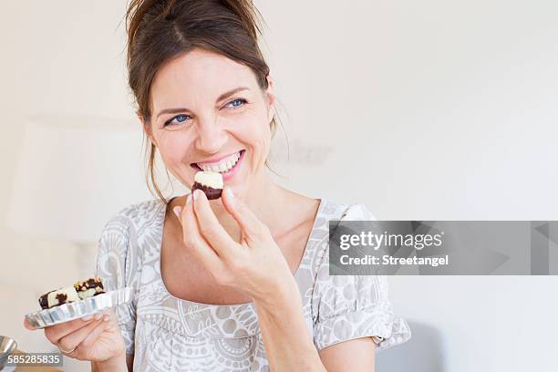 head and shoulders of mature woman holding sweet baked goods, looking away smiling - woman sweet food stock pictures, royalty-free photos & images