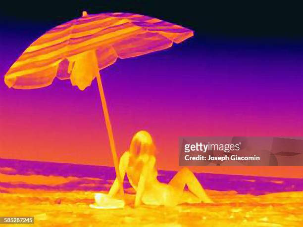 thermal image rear view of young woman sitting on beach underneath umbrella - thermal image fotografías e imágenes de stock