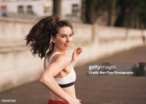 female runner looking over her shoulder whilst running - woman looking over shoulder stock-fotos und bilder