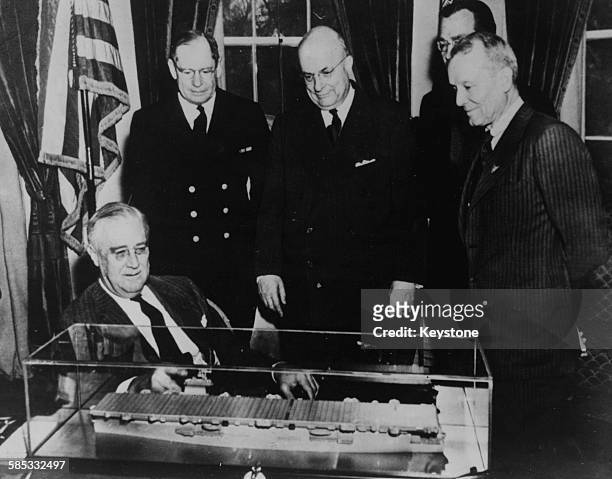 President Franklin D Roosevelt admiring a model of the new aircraft carrier-transport ships, with Rear Admiral Vickery, Henry J Kaiser, Artemus L...