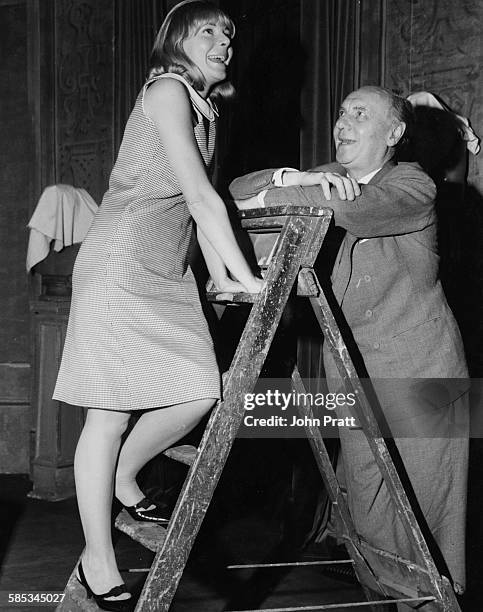 Actor Sir Ralph Richardson looking up at actress Barbara Ferris, who is climbing a step ladder, during rehearsals for the play 'Carving a Statue',...