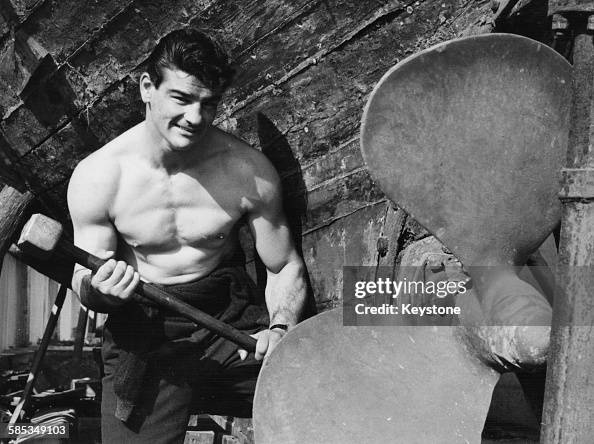 Italian boxer Giulio Rinaldi lifting a large sledge hammer as he ...