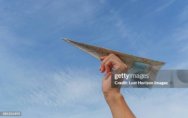 low angle view of blue sky and womans hand holding paper airplane made from map - aérodynamique photos et images de collection