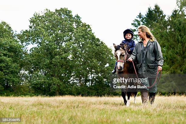 mother leading horse riding son in field - pony stock pictures, royalty-free photos & images
