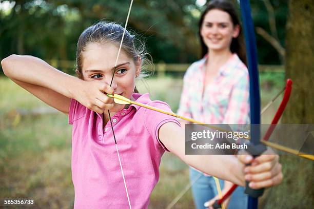 girl practicing archery aiming with bow and arrow - bogenschießen stock-fotos und bilder