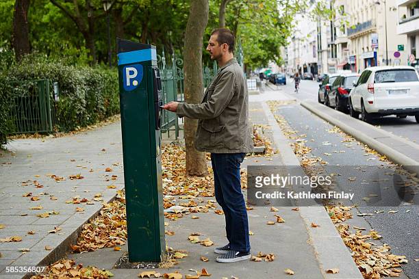 mid adult man using parking meter in street - パーキングメーター ストックフォトと画像