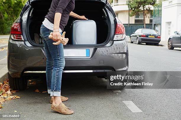 woman standing beside car, putting suitcase in open boot - neben stock-fotos und bilder