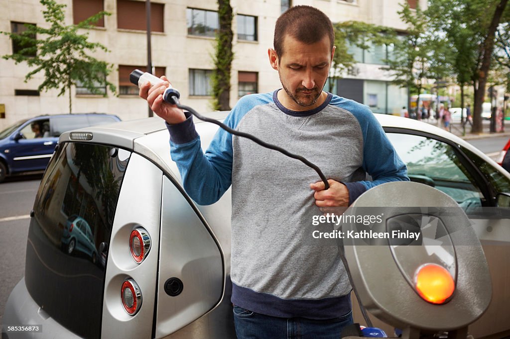 Man charging electric car on street, Paris, France