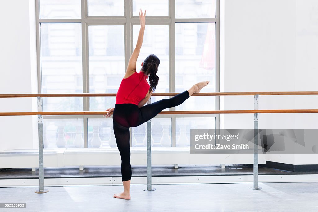 Rear view of young woman in front of window leg raised on barre