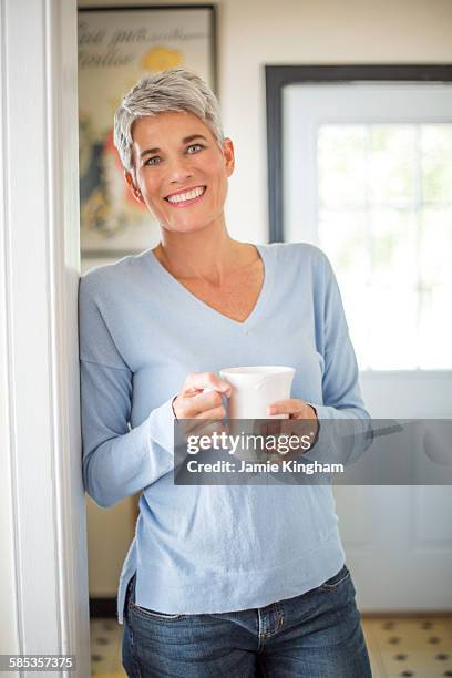 portrait of grey haired mature woman with blue eyes drinking coffee in kitchen - woman 50s blue eyes stock pictures, royalty-free photos & images