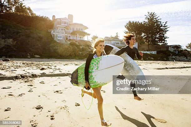 couple running towards sea, carrying surfboards - ventura california stock pictures, royalty-free photos & images