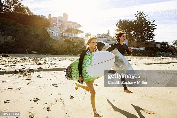 couple running towards sea, carrying surfboards - san buenaventura - fotografias e filmes do acervo