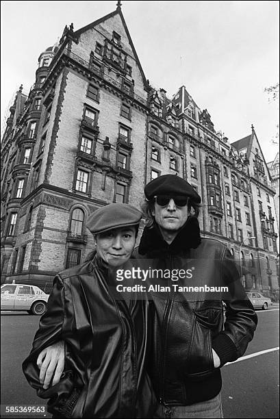 Portrait of married musicians John Lennon and Yoko Ono, both in leather jackets and berets, as they pose across the street from the Dakota...