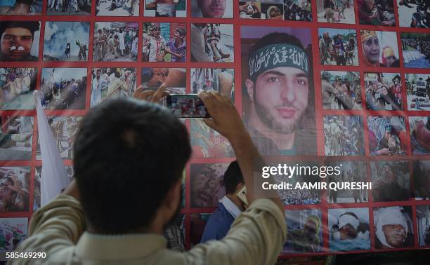 Pakistani Kashmiri protester takes a photograph of a poster bearing the image of Hizbul Mujahideen commander Burhan Wani as other protesters block a...