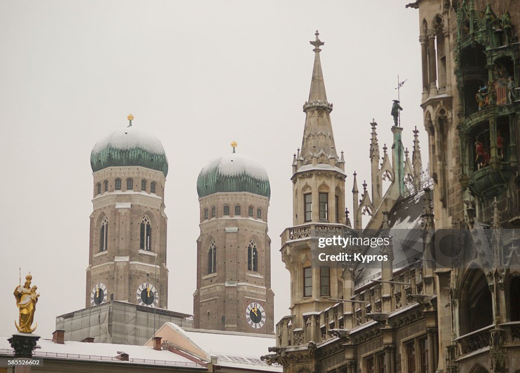 Germany, Bavaria, Munich, View Of Snow Covered Bavarian Church. Church Of Our Lady (German: Dom Zu Unserer Lieben Frau) With Tower Of The New Town Hall, Or Neues Rathaus At Marienplatz.