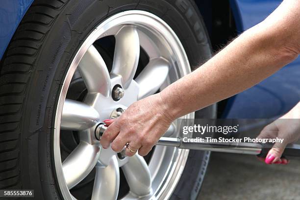 a woman changing a car wheel and tyre using a wheel brace. - cerchione in lega foto e immagini stock
