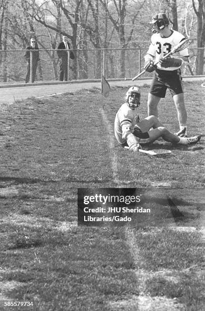 Players on a field, one of whom is sitting on the grass, during an N.C.A.A. Division one lacrosse game, in which one team was Johns Hopkins...