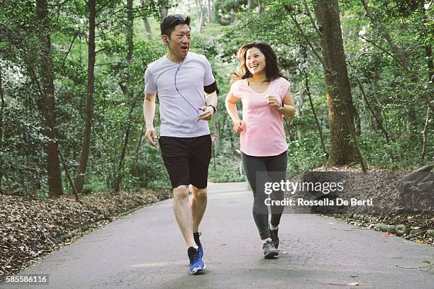 cheerful japanese couple running outdoors in a park - japanese couple stock pictures, royalty-free photos & images