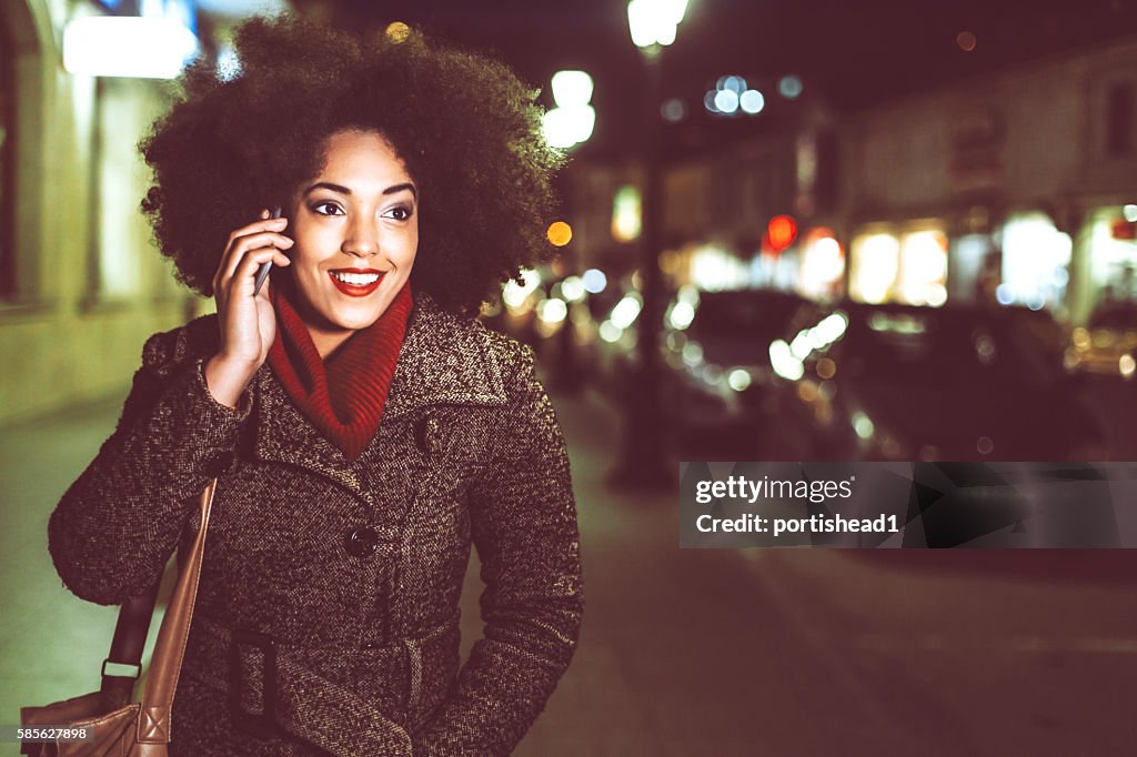 Smiling young woman using phone on street by night