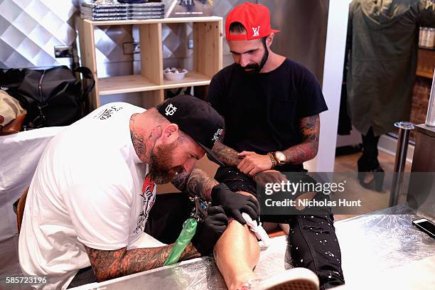 Luke Wessman tattoos a guest at the Kiehl's national LifeRide for amfAR celebration at the NYC flagship store on August 3, 2016 in New York City.