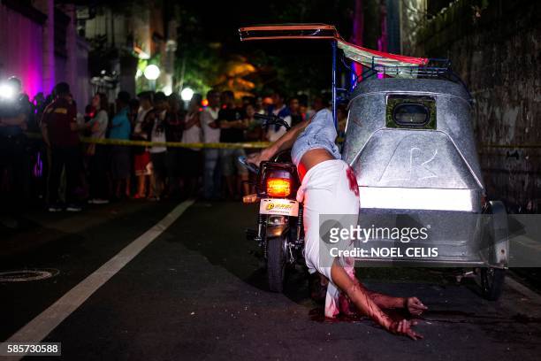 Graphic content / TOPSHOT - This photo taken on July 22, 2016 shows bystanders looking at the crime scene where the dead body of a tricycle driver...