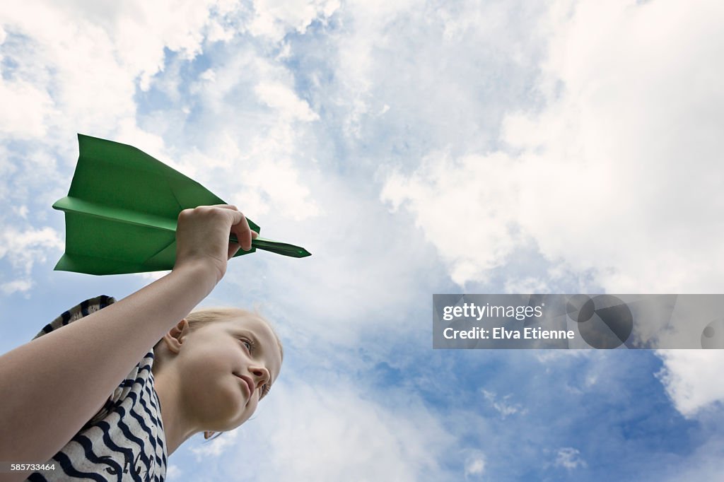 Child holding green paper aeroplane against sky