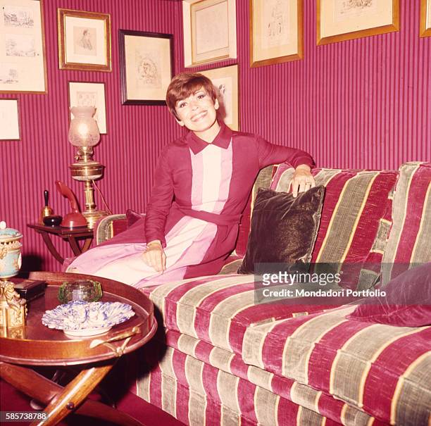 Italian actress Franca Valeri sitting and smiling on the sofa in her house. Italy, 1972