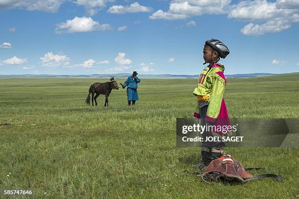 Young rider looks on next to his father and his horse after a horse race during the traditionnal Nadaam festival in a nomad camp in the Ovorkhangai...