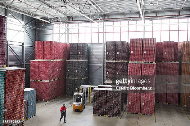 An employee passes stacks of soft drink cans on pallets in a storage area following manufacture at the Coca-Cola Co. Factory in Dongen, Netherlands,...