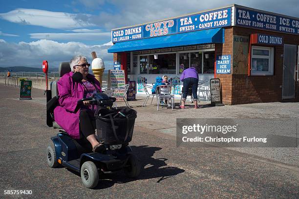 Woman rides her mobility scooter past a cafe on the promenade of Rhyl seaside resort on August 3, 2016 in Rhyl, Wales. British seaside resorts are...