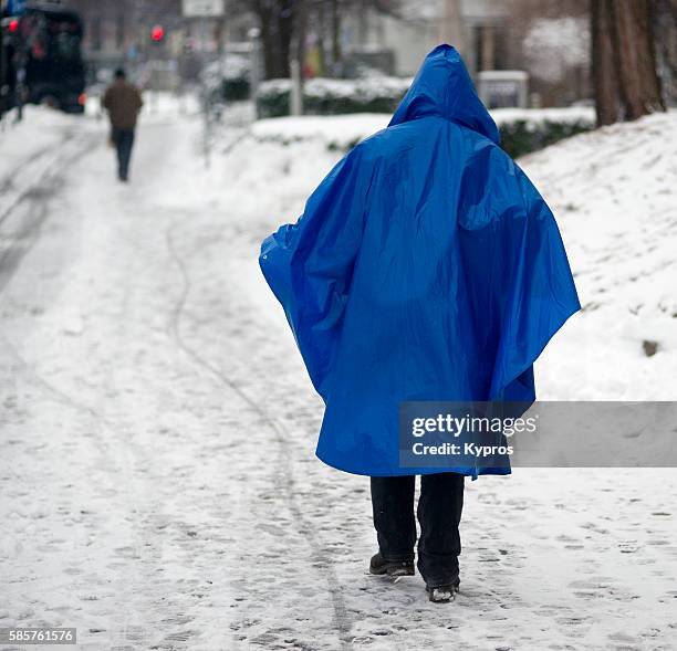 germany, bavaria, munich, view of elderly woman wearing blue raincoat walking on snow covered pavement. - frau close up portrait stockfoto's en -beelden