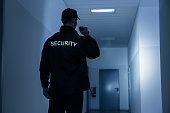 Security Guard With Flashlight In Building Corridor