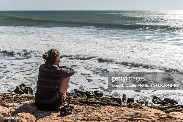 woman sitting at the coast looking at the ocean, essaouira, morocco - essaouira photos et images de collection