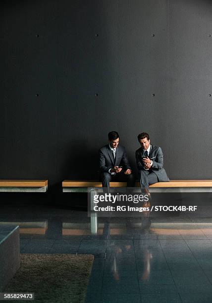 two businessmen with cell phones on bench - rf business stock-fotos und bilder