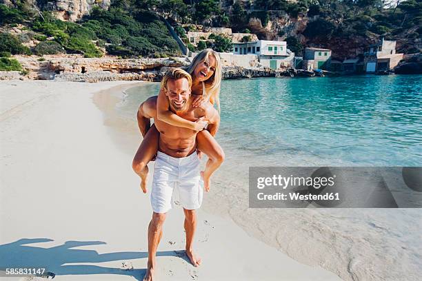 spain, majorca, man piggybacking his girlfriend at the sea - white bay stock pictures, royalty-free photos & images