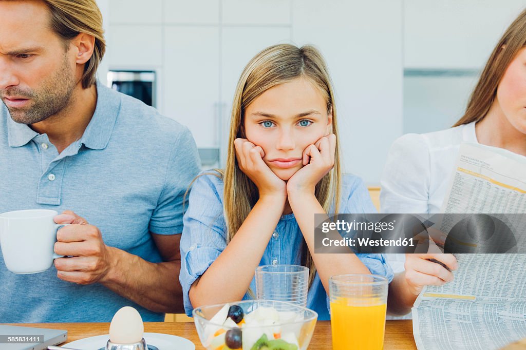 Frustrated girl with distracted parents at breakfast table