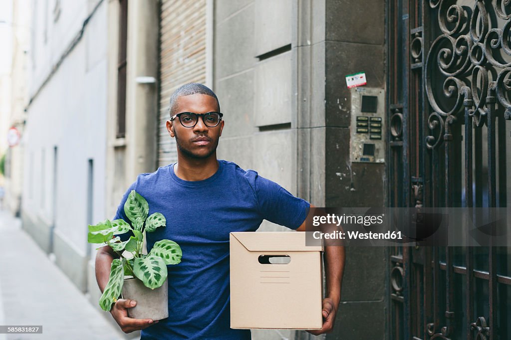 Spain, Barcelona, portrait of young man with cardboard box and foliage plant in front of a house