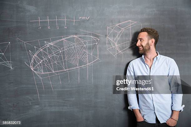 young man looking at drawing at blackboard - young man scientist stock pictures, royalty-free photos & images