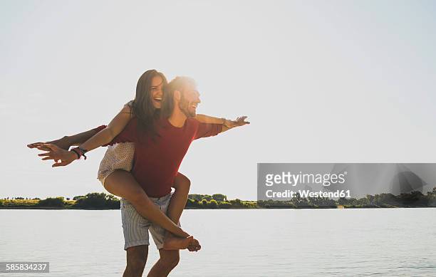 carefree young couple by the river - piggyback stock pictures, royalty-free photos & images