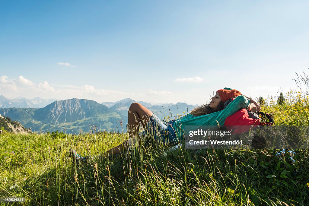 Austria, Tyrol, Tannheimer Tal, young woman lying on alpine meadow