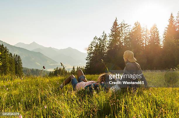 austria, tyrol, tannheimer tal, young couple resting on alpine meadow - mann lässig gras sitzen stock-fotos und bilder