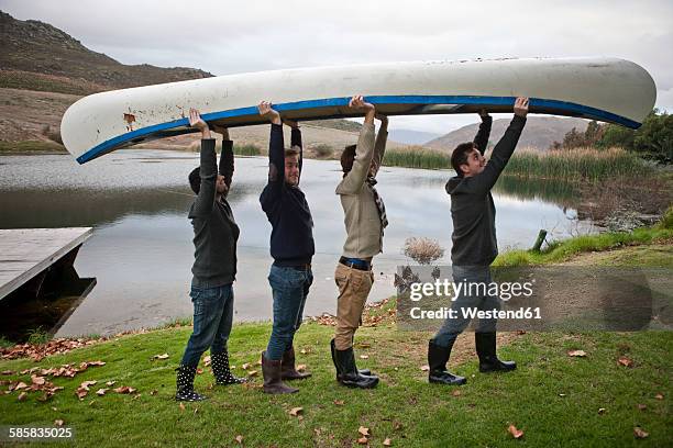 four friends carrying a canoe in front of a lake - kanu männer stock-fotos und bilder