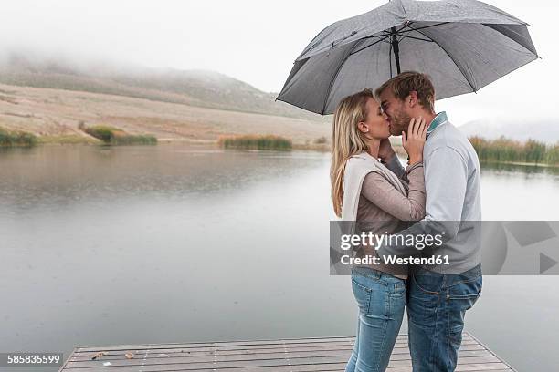 kissing couple standing in the rain with umbrella - rain kiss stock pictures, royalty-free photos & images