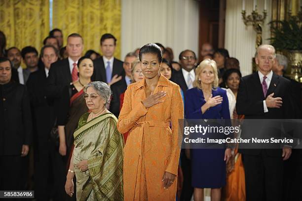 First lady Michelle Obama stands with Prime Minister of India Manmohan Singh's wife, Gursharan Kaur during the pledge of allegiance, at a welcoming...