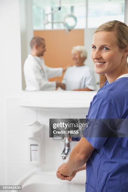 doctor washing her hands and looking at patient and another doctor - hand washing stockfoto's en -beelden