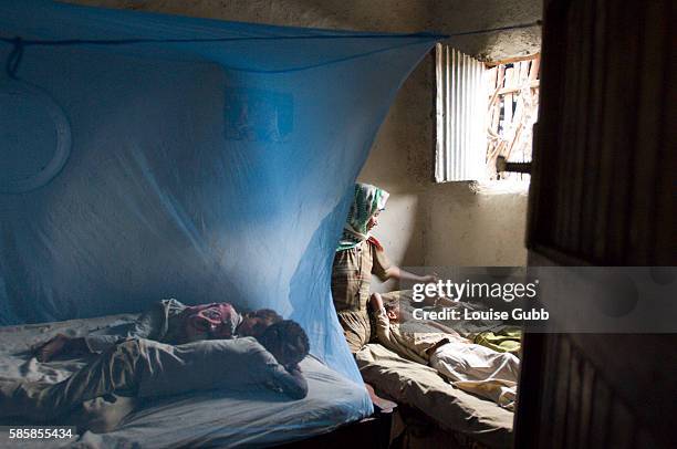 Amina Dawd strokes one of her resting children's hair as two of her other children sleep under the protective bednets. The children sleeping without...