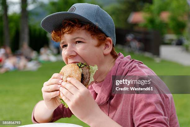 teenage boy with baseball cap eating hamburger - teenager eating stock pictures, royalty-free photos & images